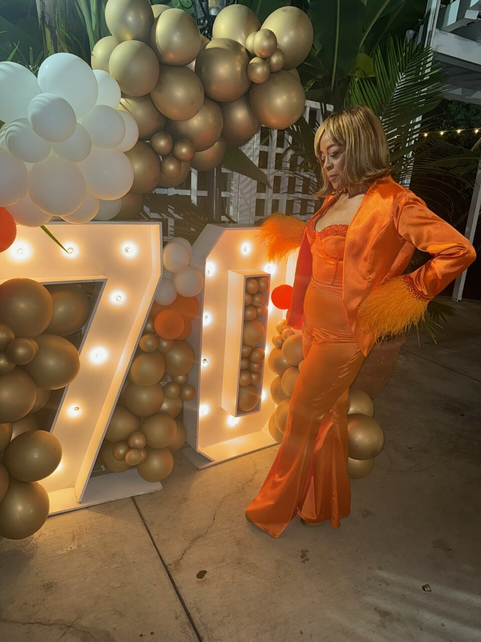 Client wearing the finished orange rhinestone birthday set with feather cuffs at a birthday celebration