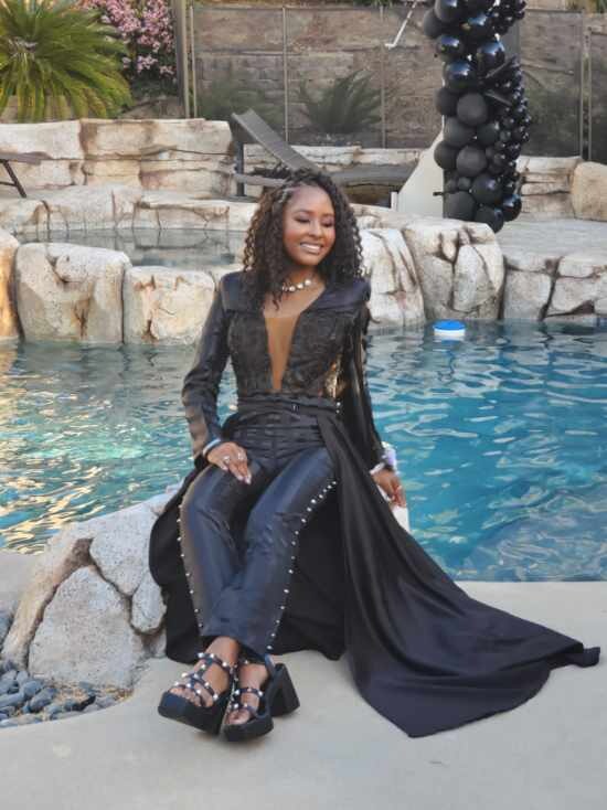 Client seated poolside wearing the finished black corset look with studded overskirt and train